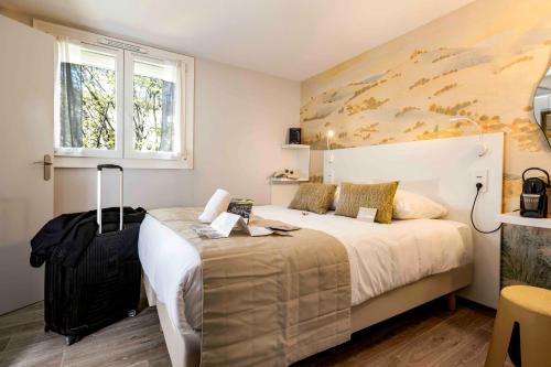 a hotel room with a bed and a suitcase at Hotel Arc-En-Ciel Colmar Contact Hotel in Colmar