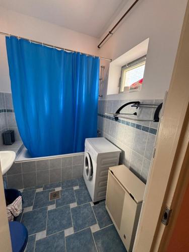 a bathroom with a blue shower curtain and a refrigerator at Holiday house Mernye in Mernye