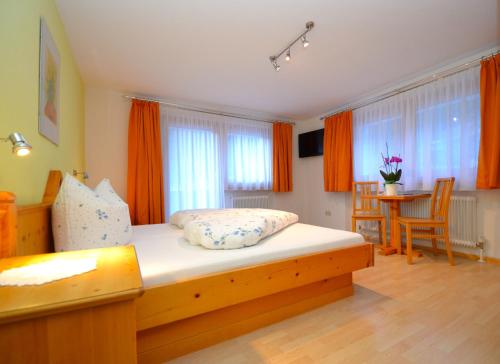 a bedroom with a bed with orange curtains and a table at Pension Christine in Gaschurn