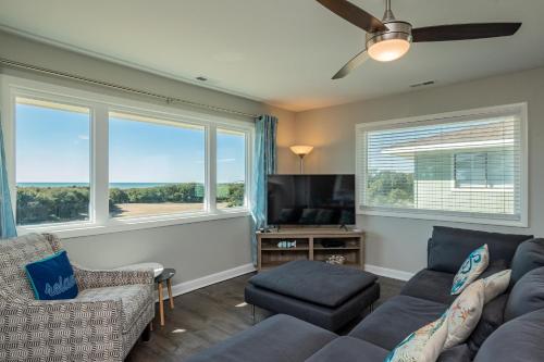 a living room with a couch and a tv and windows at Castaway by Oak Island Accommodations in Caswell Beach