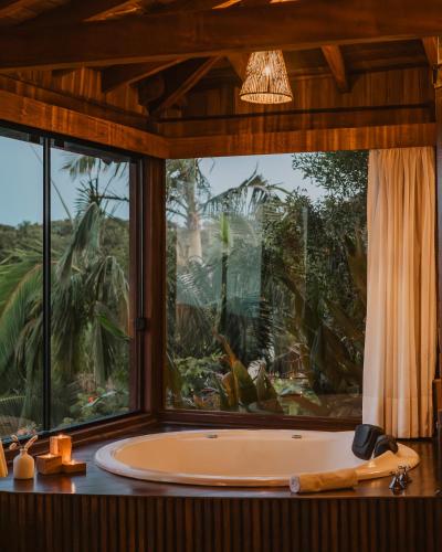 a bath tub in a room with a large window at Pousada Caminho do Rei in Praia do Rosa