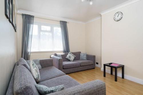 a living room with a couch and a chair and a clock at 2BR Apartment near Heathrow Airport in Wallington