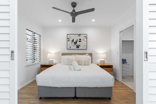 a white bedroom with a bed and a ceiling fan at Immaculate Riverside Apartment With Heated Pool in Noosaville