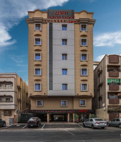a tall building with cars parked in a parking lot at Al Itqan For Serviced Apartments-الاتقان للشقق المخدومة in Jeddah