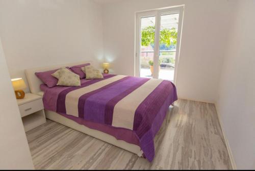 a white bedroom with a purple bed and a window at Apartman Nick in Mlini