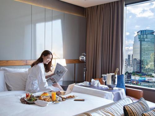a woman sitting on a bed reading a newspaper at Hilton Sukhumvit Bangkok in Bangkok