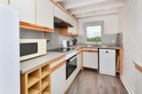a small kitchen with white cabinets and a microwave at Rhiw in Llangian