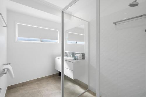 a glass shower in a white bathroom with a mirror at 1 Seaspray Avenue in Coolum Beach