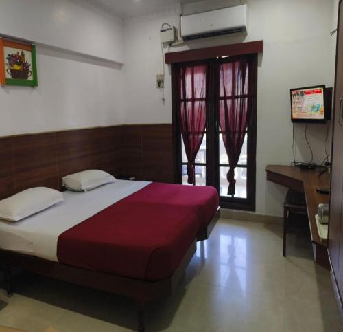 a bedroom with a bed and a desk and a window at Ajantha Beach Guest House in Pondicherry