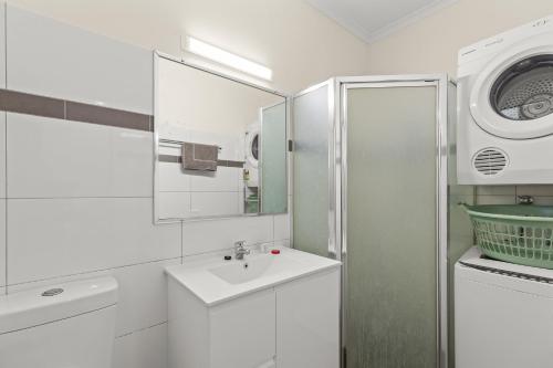 a white bathroom with a sink and a washing machine at Cable Beachside Apartments in Broome