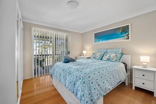 a bedroom with a bed with a blue bedspread and a window at Seabreeze Cottage in Manyana