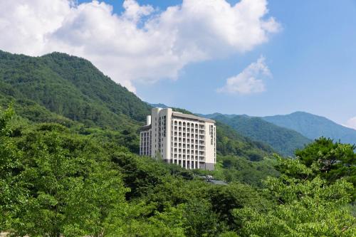 a large white building on a hill with trees at KensingtonResort JirisanHadong in Hadong
