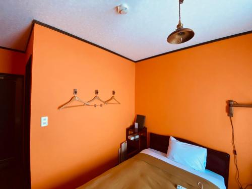 a bedroom with an orange wall with a bed and hangers at HOTEL Saboten Apartment in Miyoshi