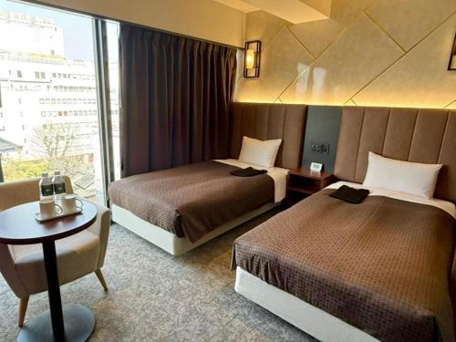 a hotel room with two beds and a table at Place Hotel Ascot in Kumamoto