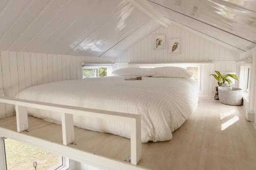 a white bedroom with a large bed in a attic at Kookaburra Tiny House by Tiny Away in Palmwoods