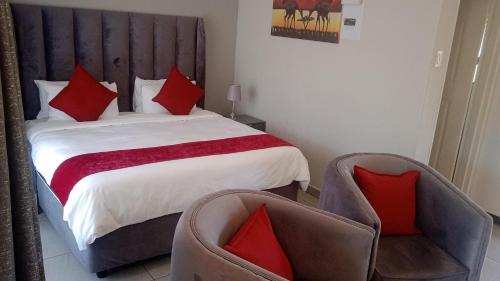 a bedroom with a bed with red pillows and two chairs at Tree Tops Game Resort in Magomba