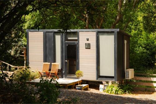a tiny house in the woods with two chairs at Tranquility Tiny House by Tiny Away in Owaka