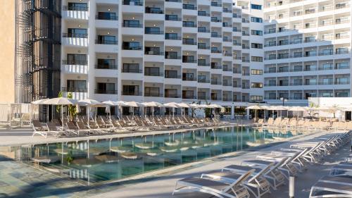 a pool with chairs and umbrellas in front of a building at Hotel Vibra Beverly Playa in Paguera