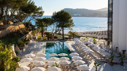 an outdoor pool with umbrellas and chairs and the ocean at Hotel Vibra Beverly Playa in Paguera