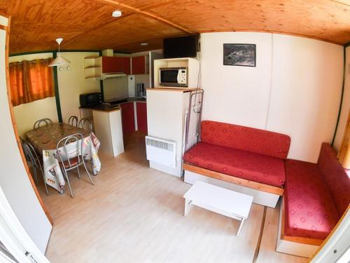 a small room with a red couch and a kitchen at Camping Onlycamp l'Astrée in Bourg-Argental