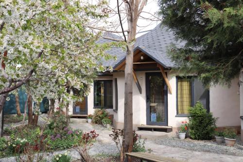 a white house with trees and flowers in front of it at Happy Nomads - Modern Yurt Cottages & Breakfast in Karakol
