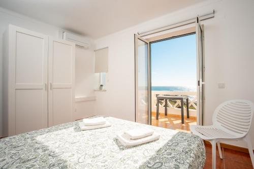 a white bedroom with a bed and a view of the ocean at Casas do Zé Zambujeira do Mar in Zambujeira do Mar