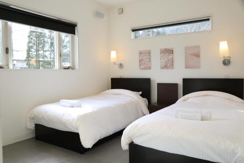two beds in a room with two windows at Powdersuites by The Hakuba Collection in Hakuba