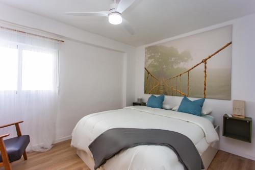 a white bedroom with a large bed with blue pillows at Lighthouse Cullera Penthouse in Cullera