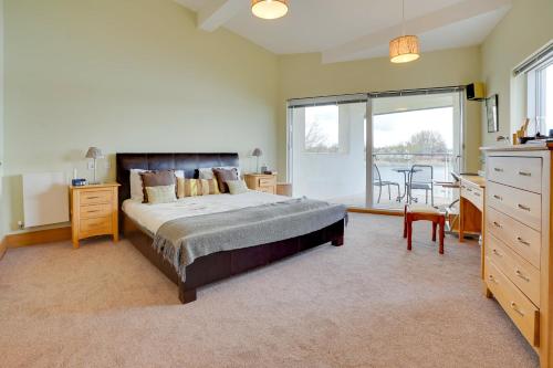 a bedroom with a bed and a desk and a balcony at Squirrels Leap Lake Views with Spa Access, Lower Mill Estate in Somerford Keynes