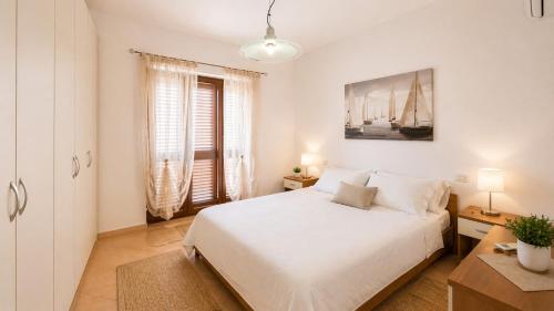 a white bedroom with a bed and two windows at Casa Rosada Alghero in Alghero
