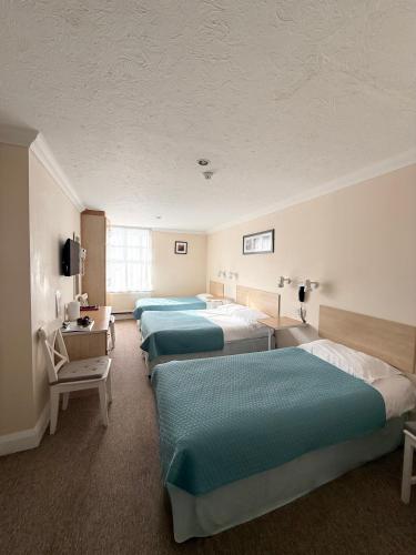 a hotel room with four beds and a chair at Eastbourne Riviera Hotel in Eastbourne