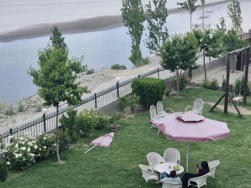 a table and chairs with a pink umbrella in the grass at Hotel Blangsa Indus View in Skardu