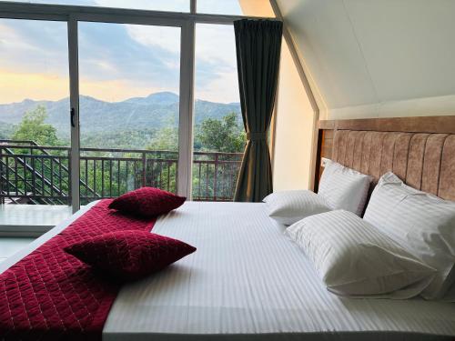 a bed with red and white pillows in front of a window at Wilmora in Ramakkalmedu