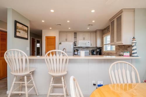 a kitchen with two white bar stools and a table at Fish Tales by Oak Island Accommodations in Oak Island