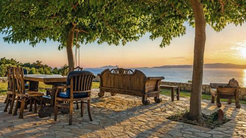a group of benches and a table with a view of the water at Panoramic Sea View Wooden Cottage Ratzakli, Kefalonia in Ratzaklíon