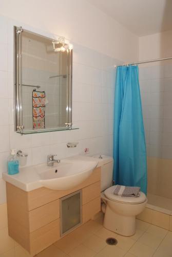 a bathroom with a sink and a toilet with a blue shower curtain at Secret Arcadia Bay - Maisonette Breathtaking sea & mountain view-Just on the beach in Áyios Andréas Arkadias