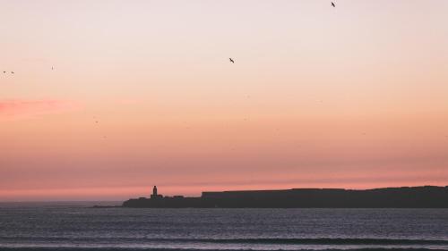 a lighthouse on an island in the ocean at sunset at Riad Zahra in Essaouira