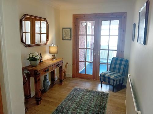 a living room with a table and a chair and a mirror at Abbeyside Cottage in Kelso