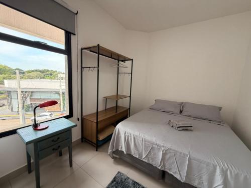 a bedroom with a bed and a desk and a window at Studio Smart Ponte da Amizade in Foz do Iguaçu