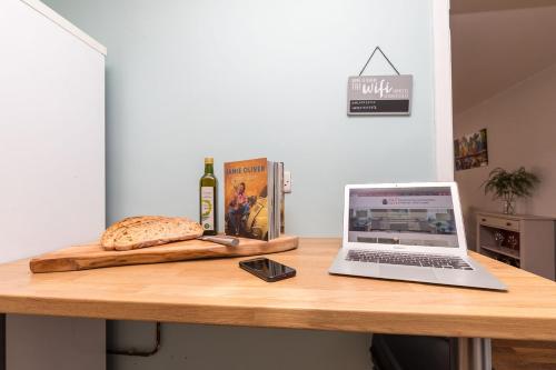 a laptop computer sitting on a wooden table with a bread and a bottle of wine at Rivermead - Gorgeous 3 Bed Maisonette with Patio in Horsham