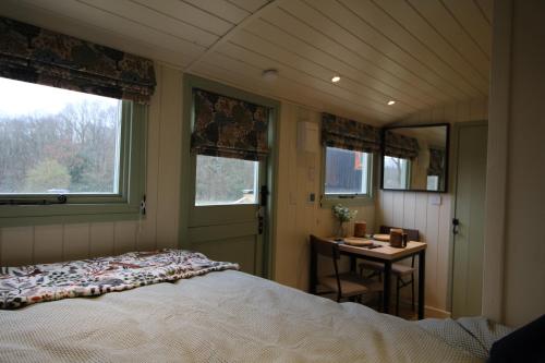 a bedroom with a bed and a table and windows at Spinney Wood Glamping, Oak Hut in Bewdley