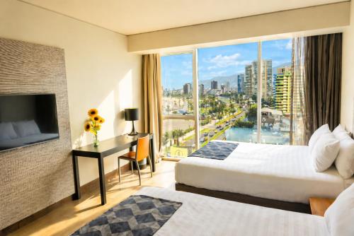 a hotel room with two beds and a desk with a window at Hotel Terrado Cavancha in Iquique