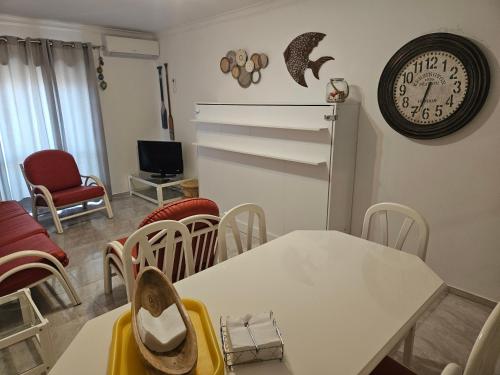 a living room with a table and a clock on the wall at Âncora Guest House in Monte Gordo