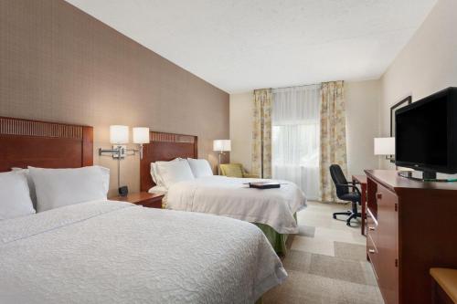 a hotel room with two beds and a flat screen tv at Hampton Inn Burlington - Colchester in Burlington