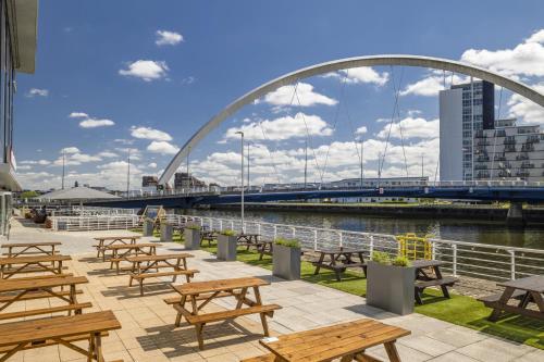a group of picnic tables with a bridge in the background at Hilton Garden Inn Glasgow City Centre in Glasgow