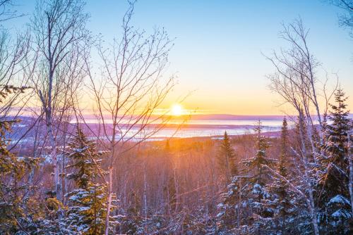 a winter sunset over a snowy forest with the sun setting at Nørdika Charlevoix in Baie-Saint-Paul