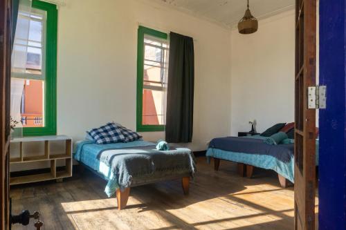 a bedroom with two beds and a chair and a window at Gatalegre Hostel in Valparaíso