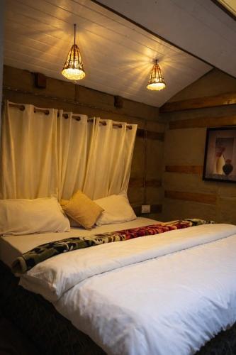 two beds in a room with white sheets and two lights at The Crystal Cabin in Jibhi