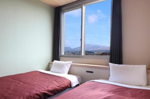 two beds in a room with a window at Gogaku Hotel in Aso