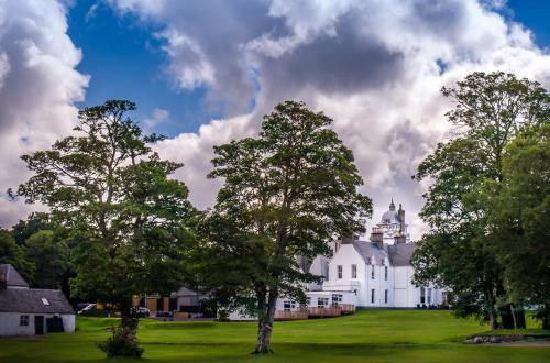 a large white house with trees in the foreground at Skeabost House Hotel in Portree